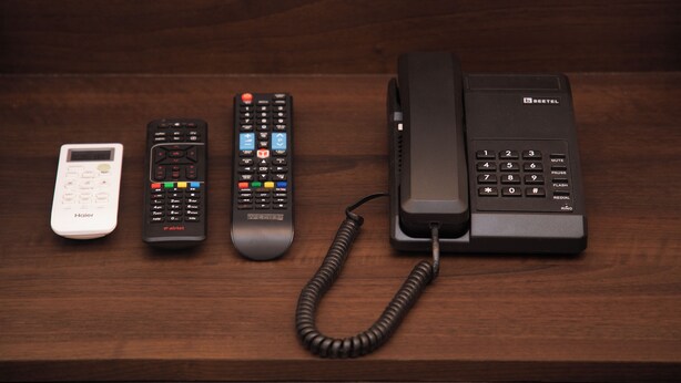 Una superficie de madera con cuatro controles remotos y un teléfono.