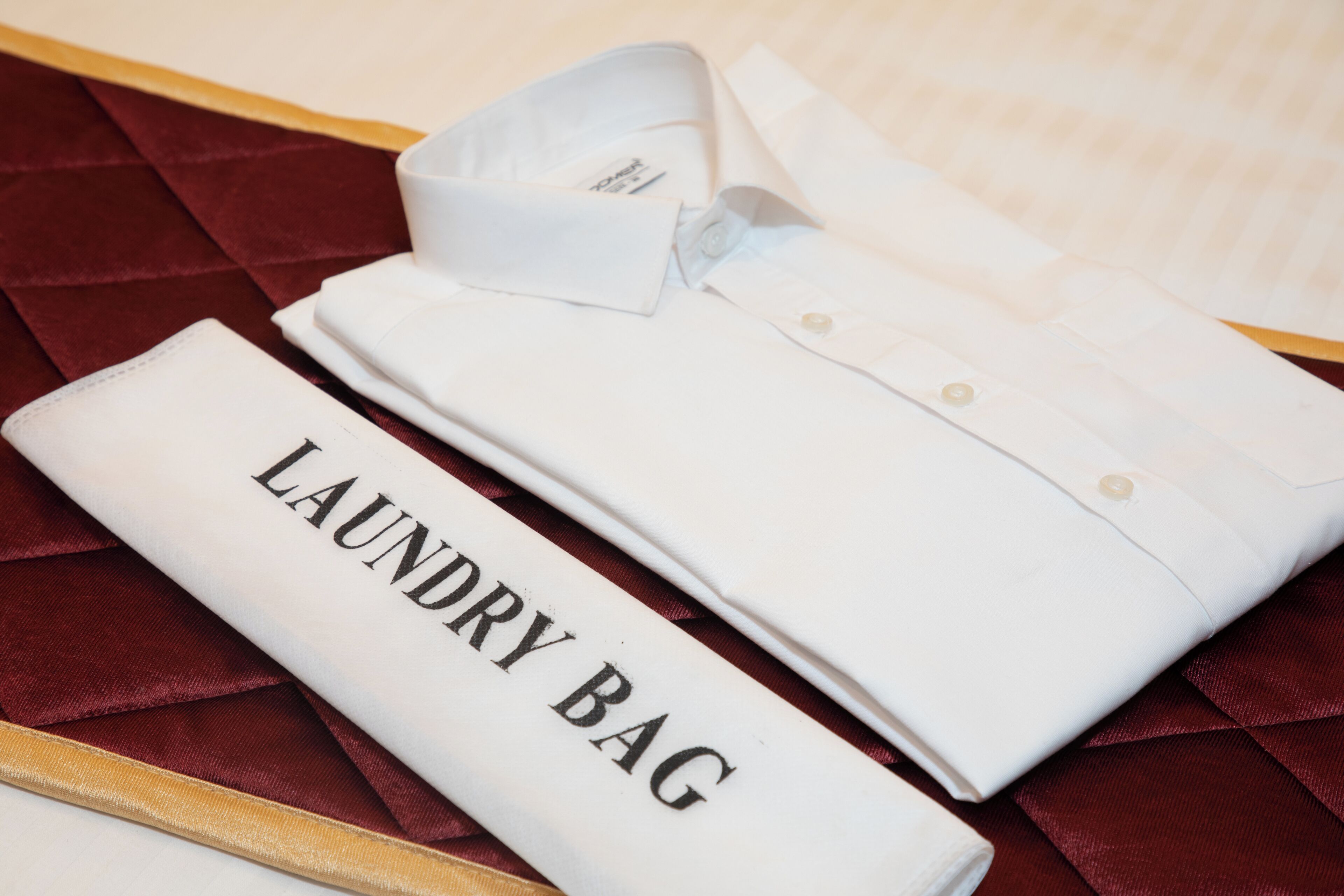 A neatly folded white shirt with a label reading "LAUNDRY BAG" on a red velvet surface.