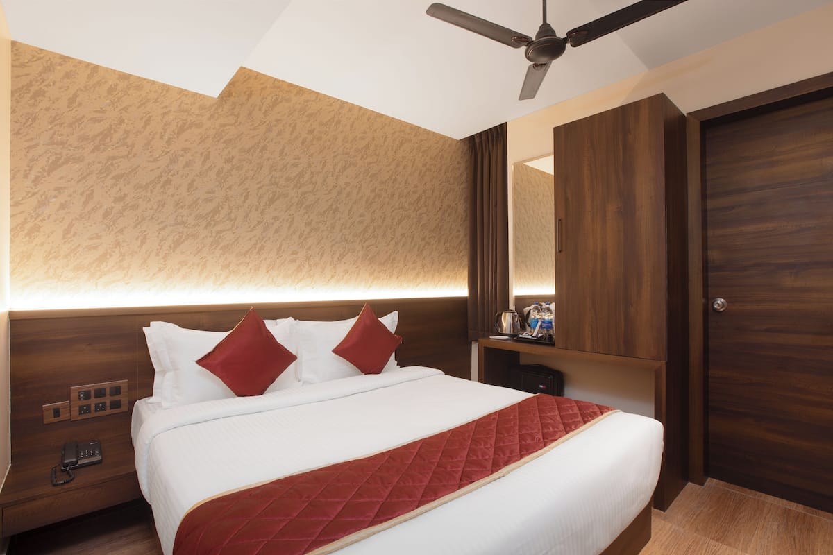 A hotel room with a bed, a ceiling fan, a nightstand, and a wooden wardrobe.