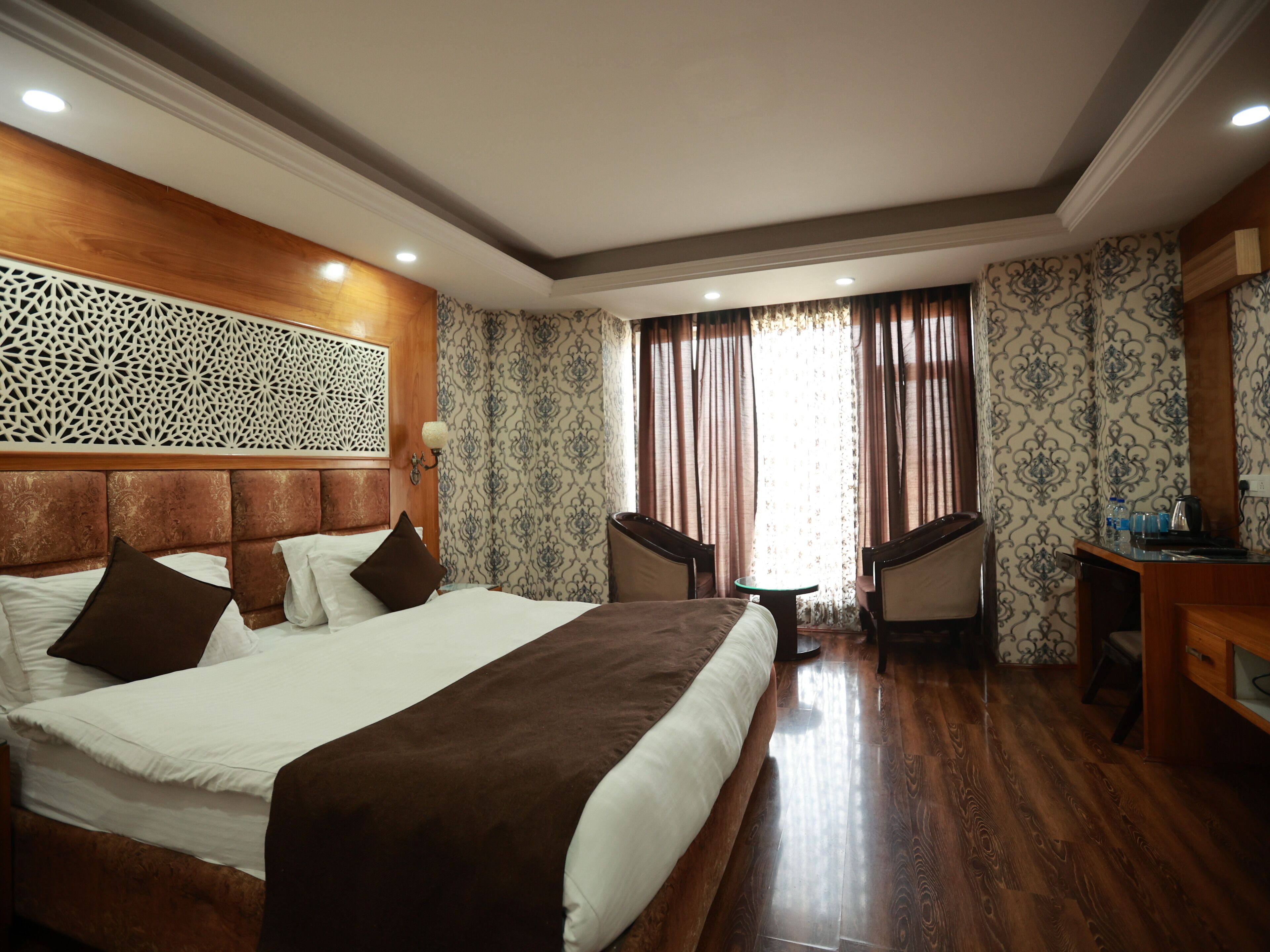 A hotel room with a large bed, two chairs, a small table, and a decorative wall panel.