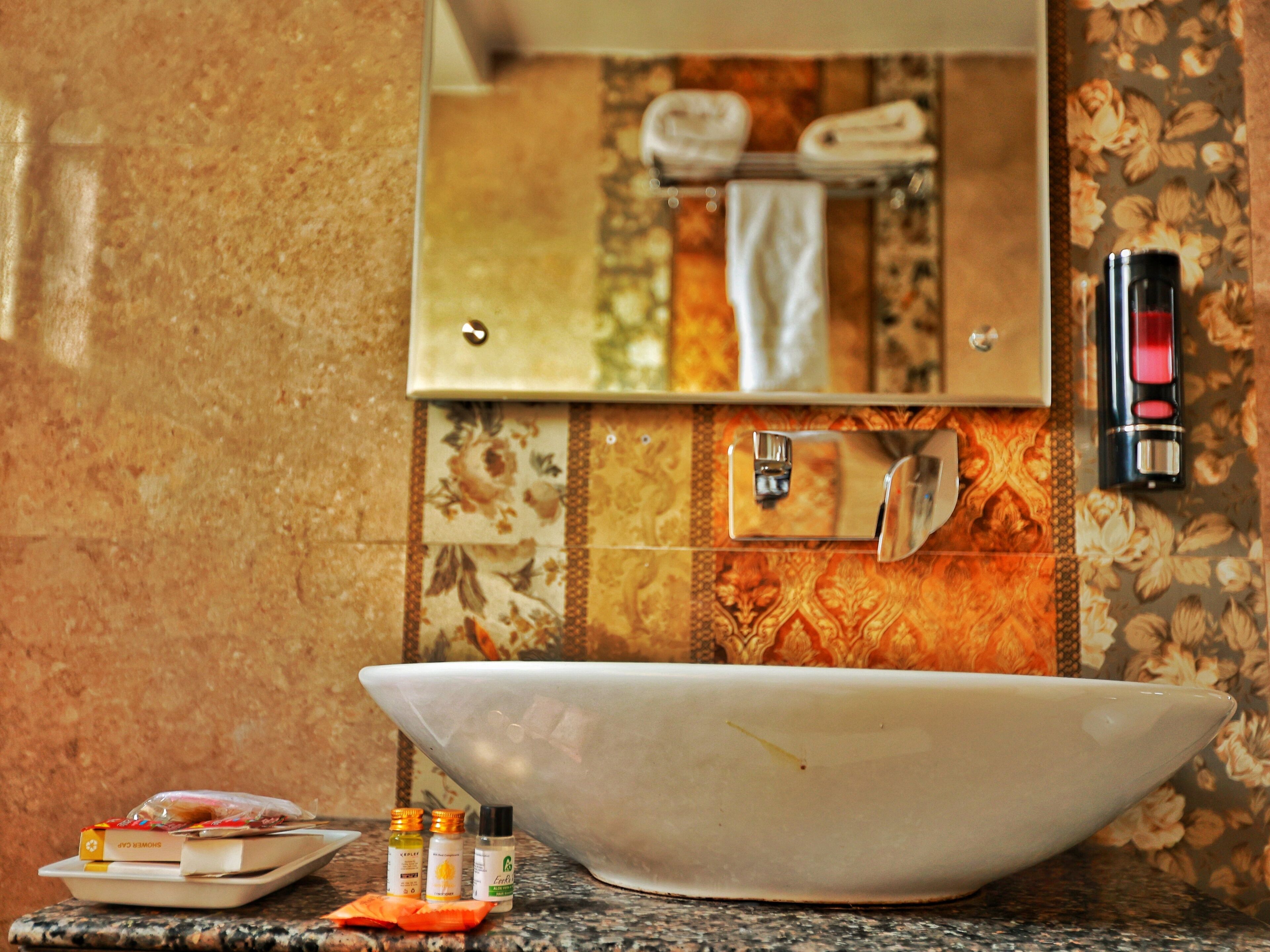 A bathroom with a large white vessel sink, a mirror, a towel rack, and a soap dispenser.