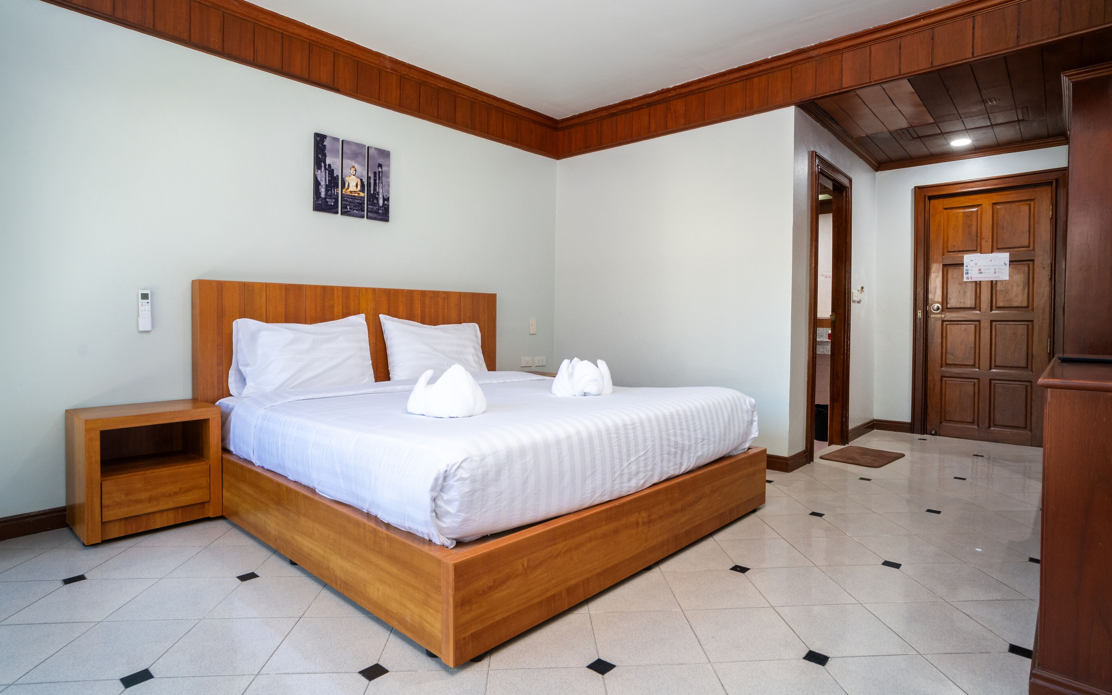 Une chambre à coucher bien rangée, avec un lit en bois, une table de chevet, un panneau de commande fixé au mur et une porte avec une pancarte.