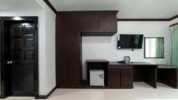 A hotel room with a dark wooden wardrobe, a small refrigerator, a desk, a television, and a bed.