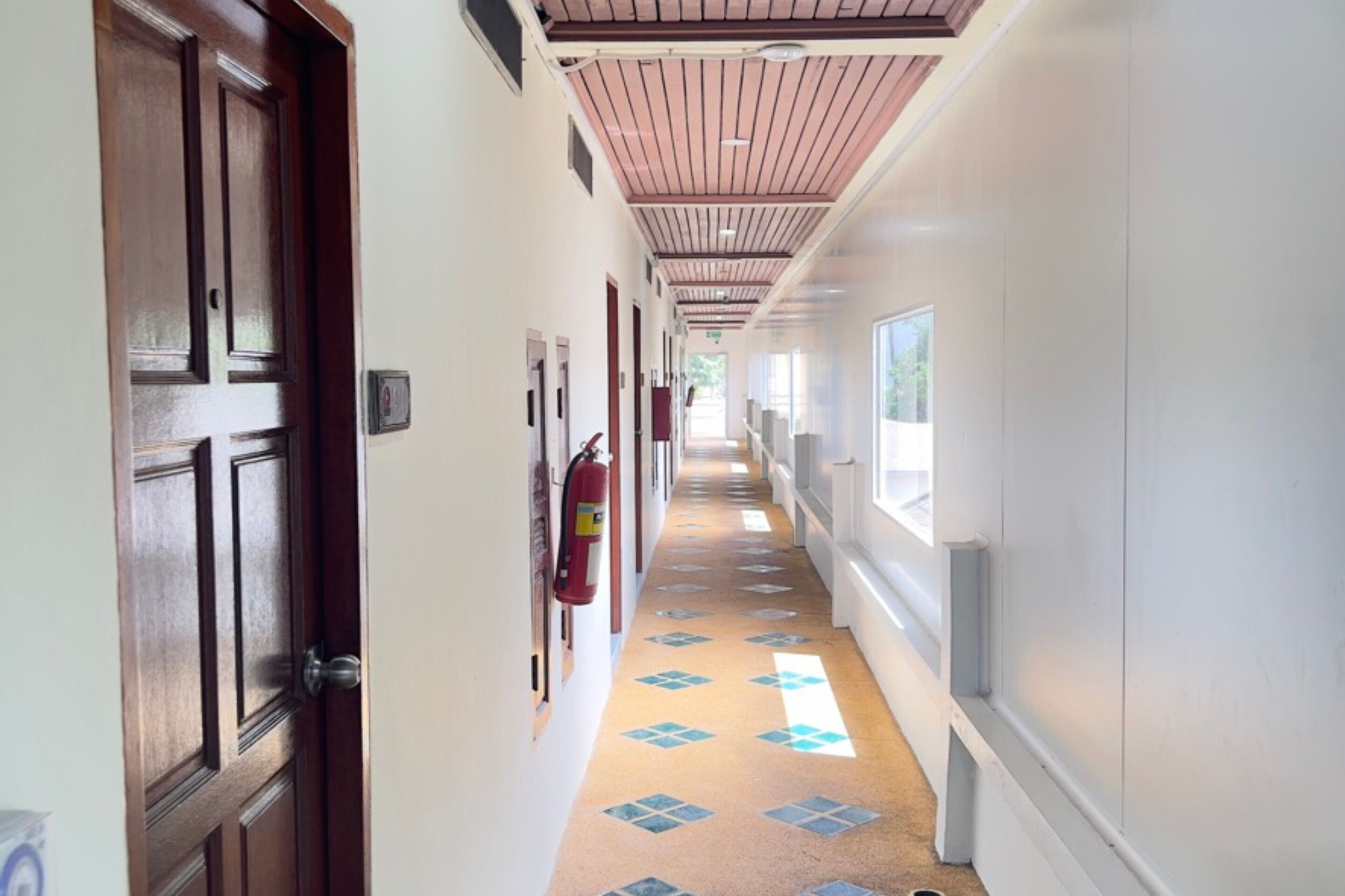 Un pasillo de hotel con puertas de madera, un extintor y un suelo estampado.