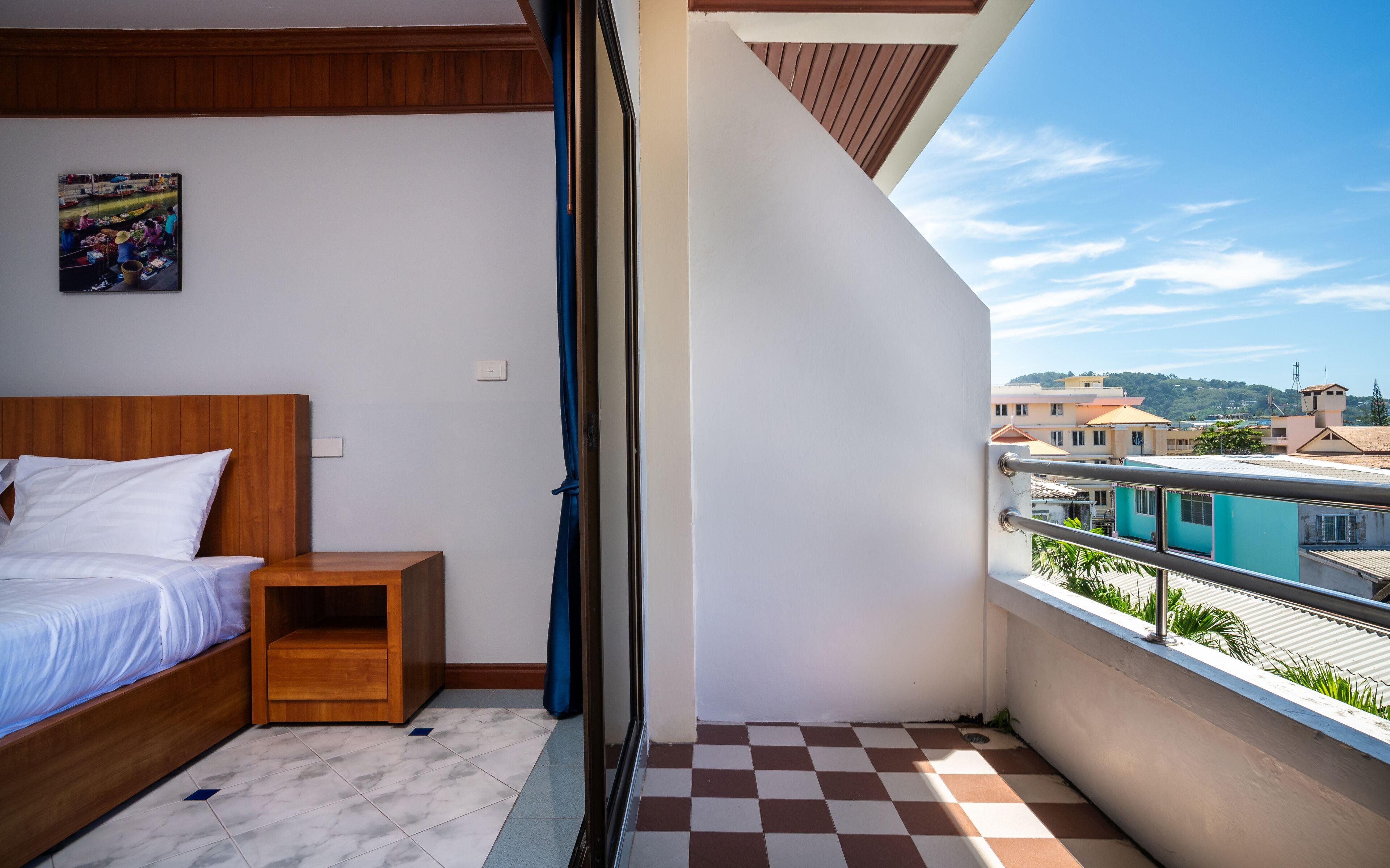 A bedroom with a bed, nightstand, and a view of the city through a balcony.