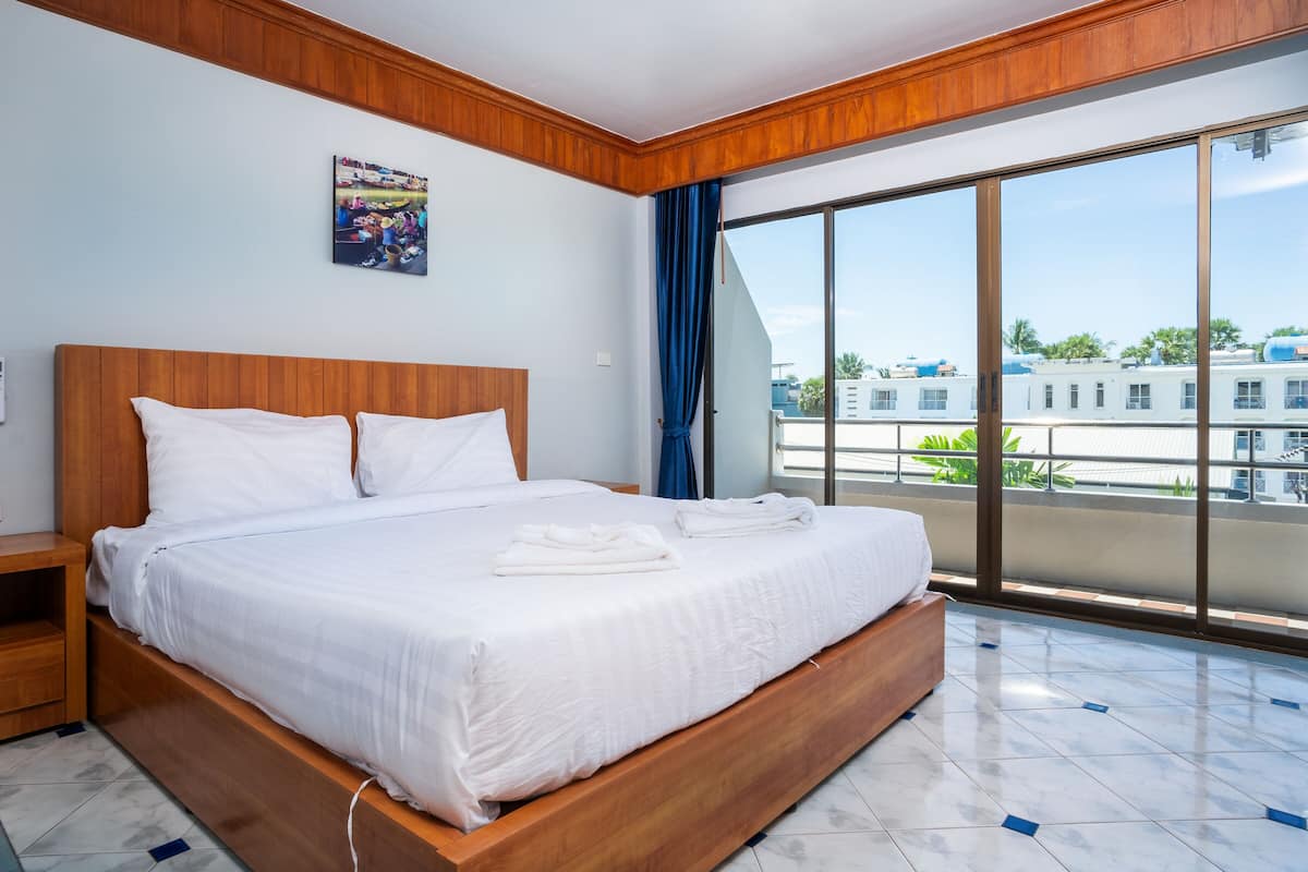 A hotel room with a large bed, wooden headboard, a painting on the wall, and a view of buildings through large windows.