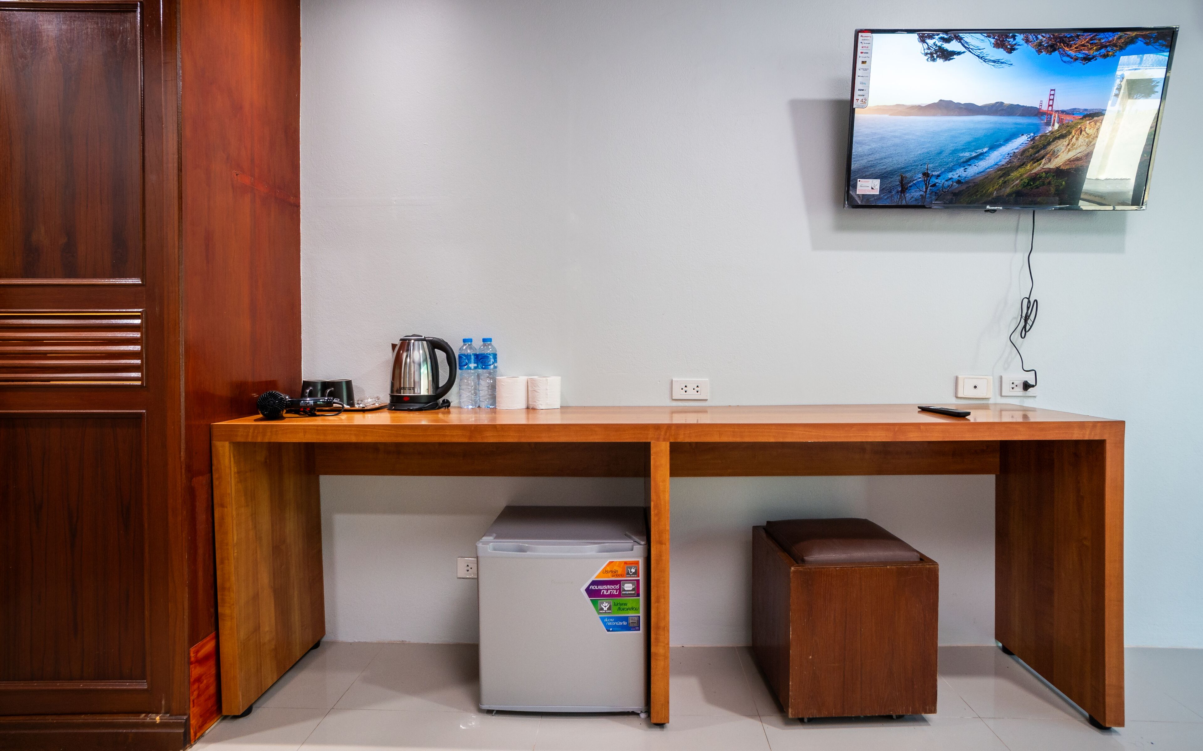 Een houten bureau met een koelkast, koffiezetapparaat en afstandsbediening. Een televisie is aan de muur boven het bureau bevestigd.