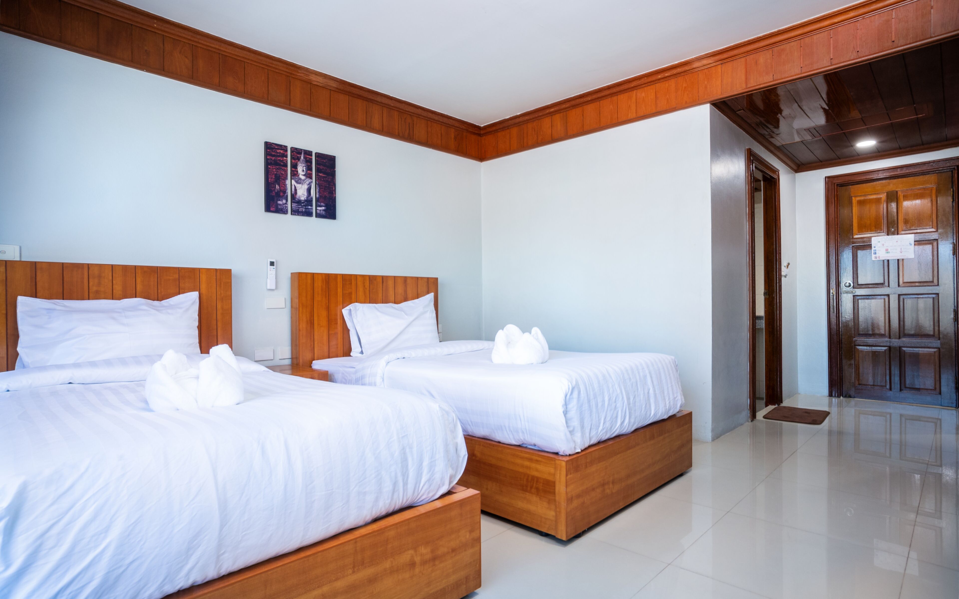 A hotel room with two wooden beds, white bedding, a wooden ceiling, and a door leading to another room.