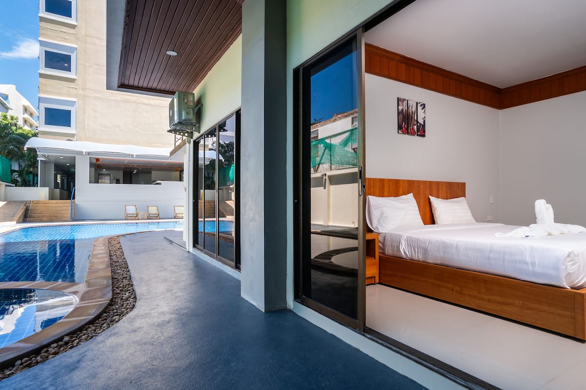 A modern hotel room with a large bed, a private balcony with a pool, and a view of the cityscape.