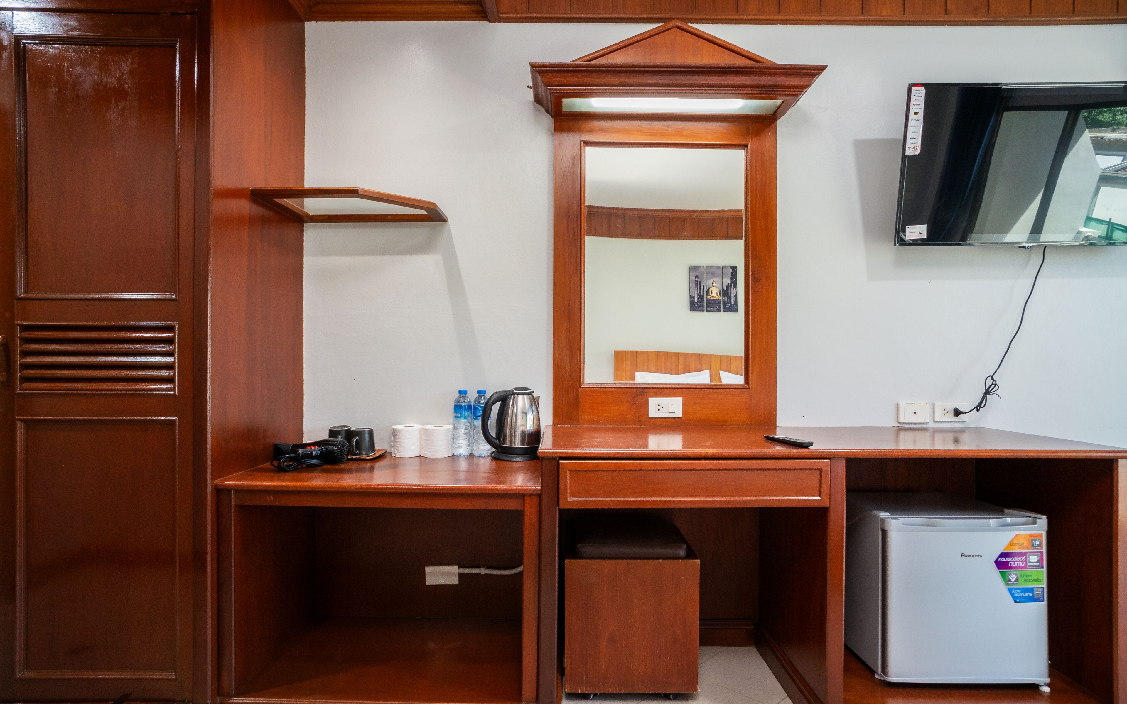 A wooden desk with a mirror, a kettle, and a refrigerator.
