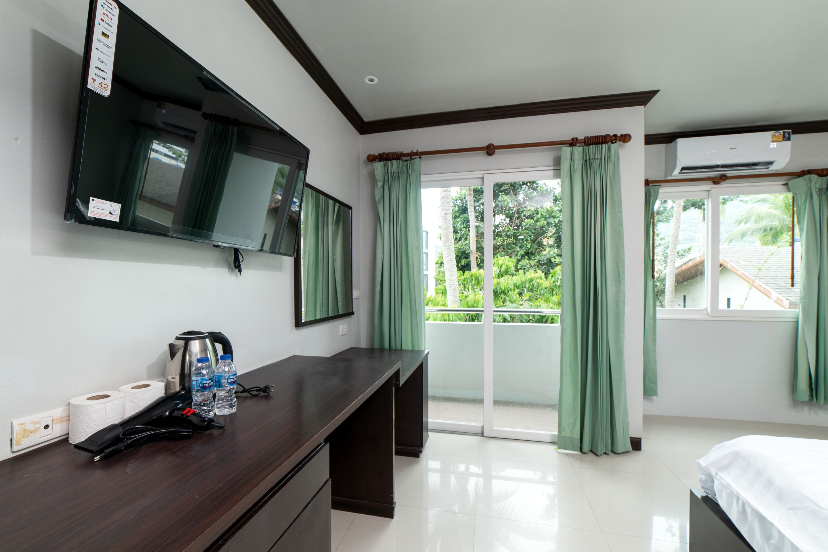 Habitación de hotel con televisor de pantalla plana, escritorio con artículos de aseo, cama y puerta corrediza de vidrio al exterior.