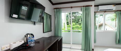 Habitación de hotel con televisor de pantalla plana, escritorio con artículos de aseo, cama y puerta corrediza de vidrio al exterior.
