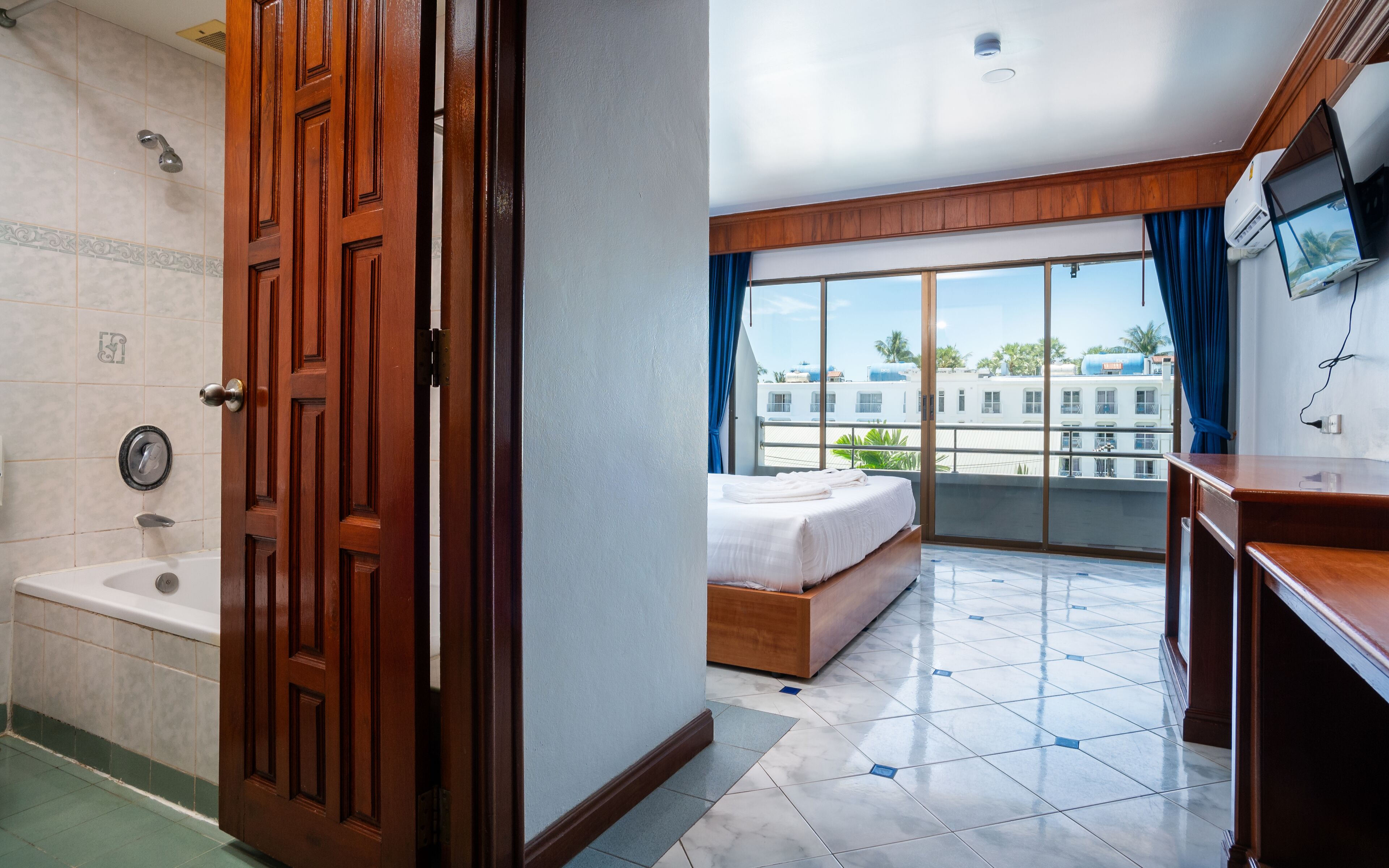 A hotel room with a bathroom, a balcony with a bed, and a TV.
