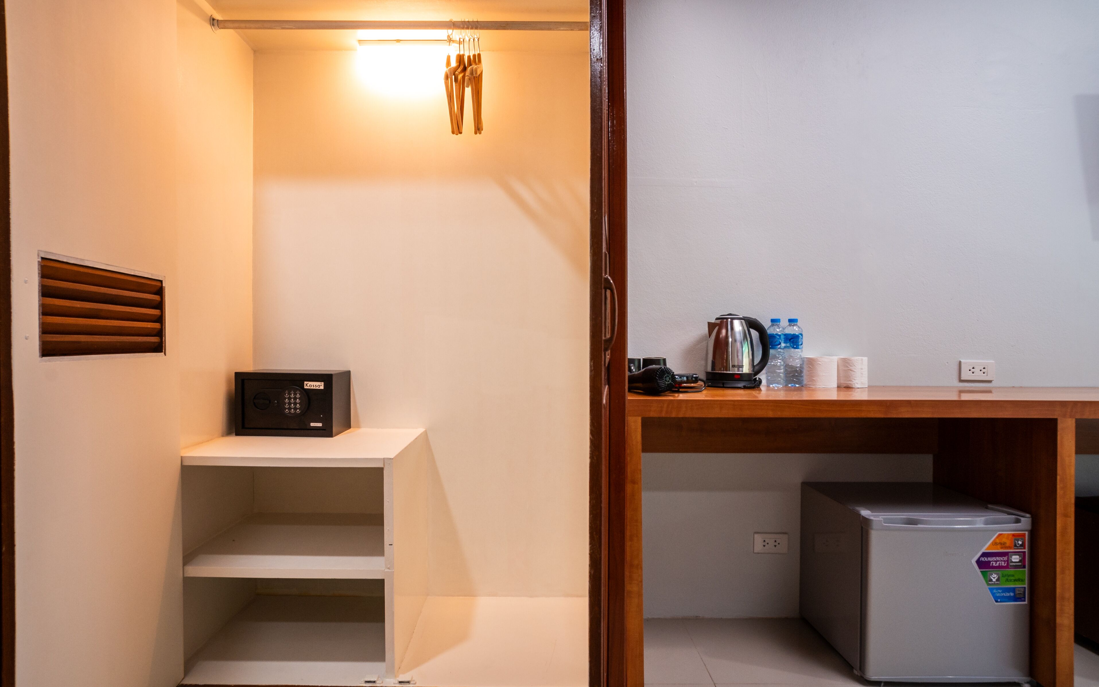 A compact kitchenette with a small refrigerator, a kettle, and a water bottle.