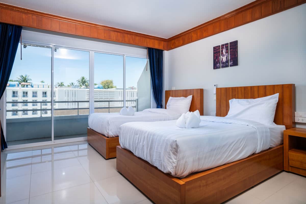 A hotel room with two beds, a balcony with a view of buildings and palm trees, and a wooden ceiling.