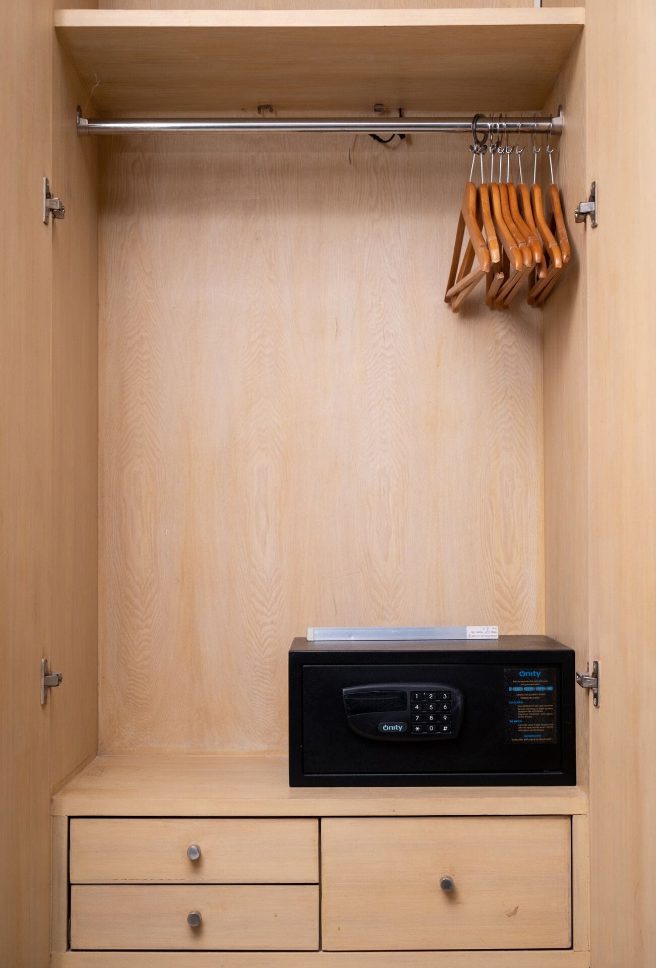 Ein Holzschrank mit einem schwarzen elektronischen Gerät darauf, zwei Schubladen und einer Kleiderstange mit Holzaufhängern.