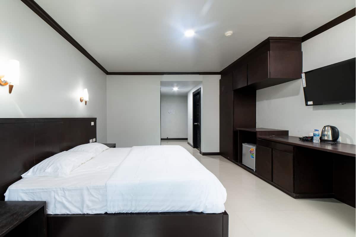 A modern hotel room with a large bed, a desk, a flat-screen TV, and a minibar.