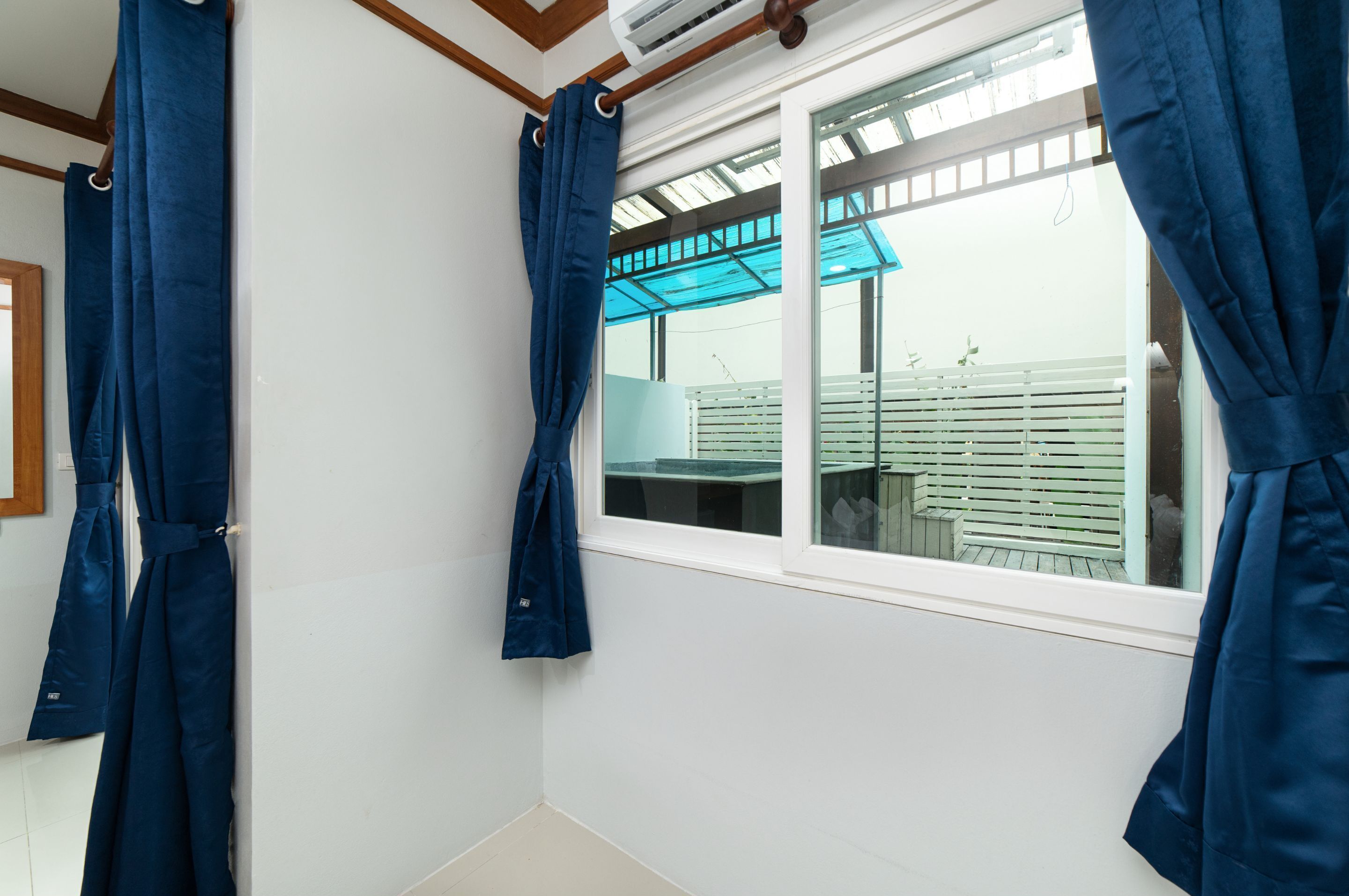 Una habitación con un ventanal grande, paredes blancas y cortinas azules.