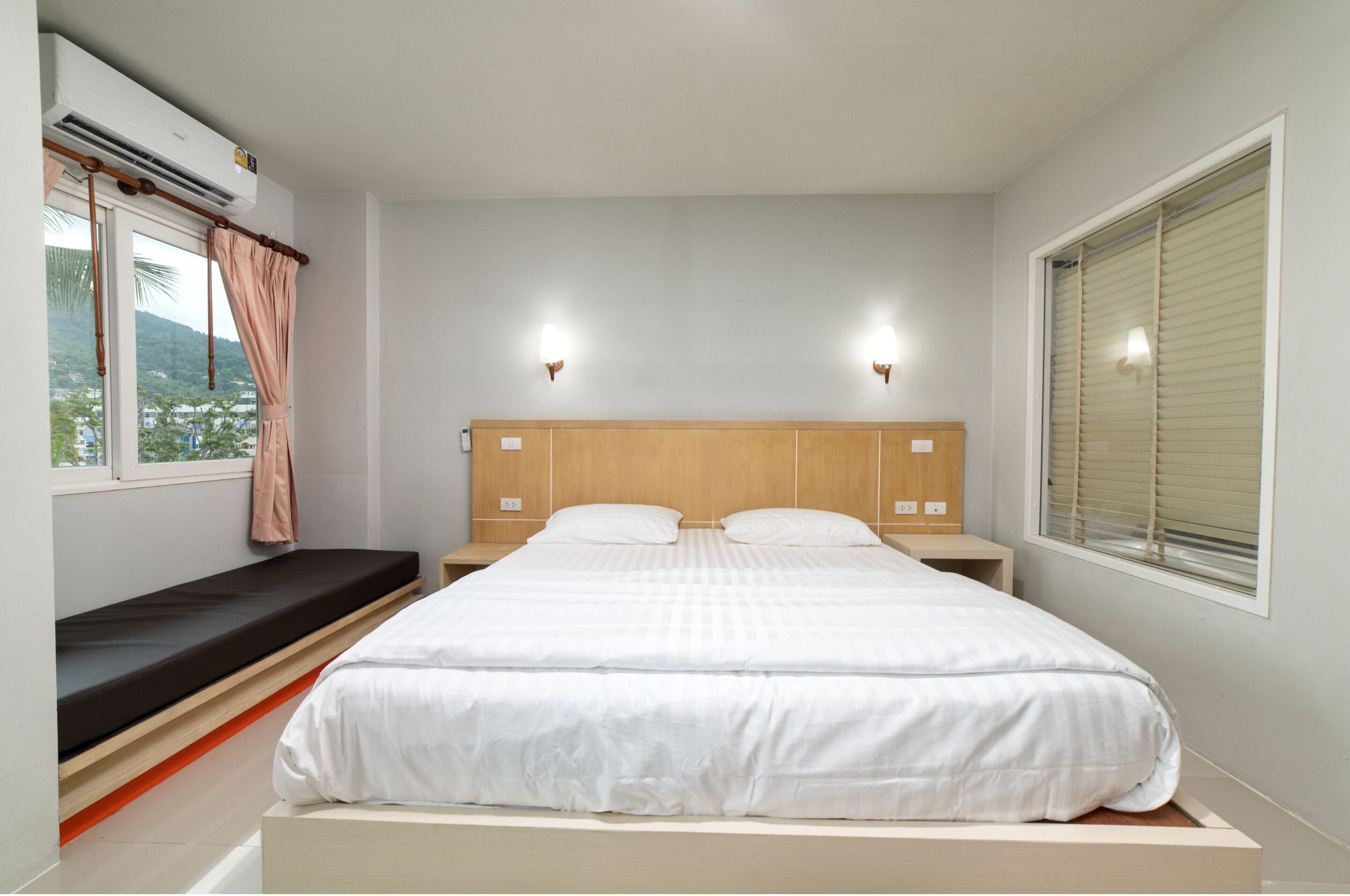 Un dormitorio con una cama grande, un banco junto a la ventana y dos luces fijadas en la pared.