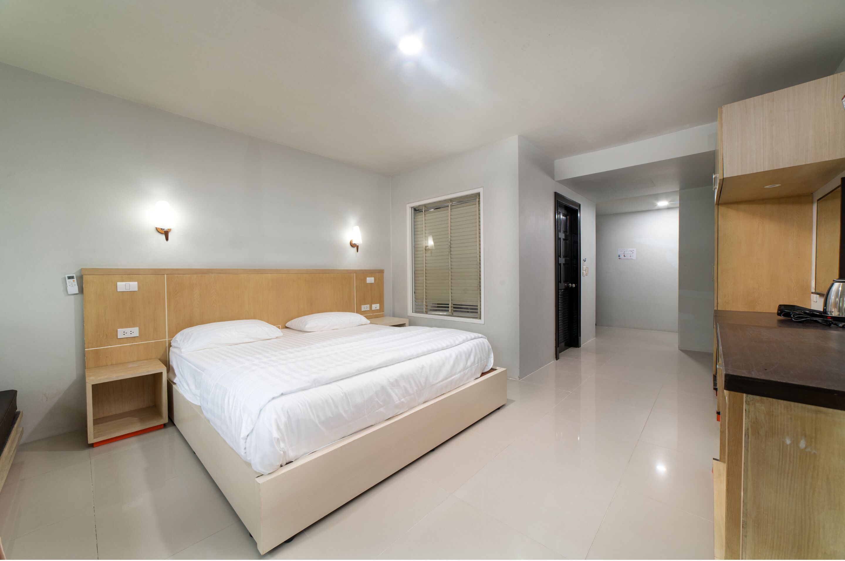 Une chambre moderne avec un lit en bois, des tables de chevet, une fenêtre avec des stores et une porte donnant sur une autre pièce.