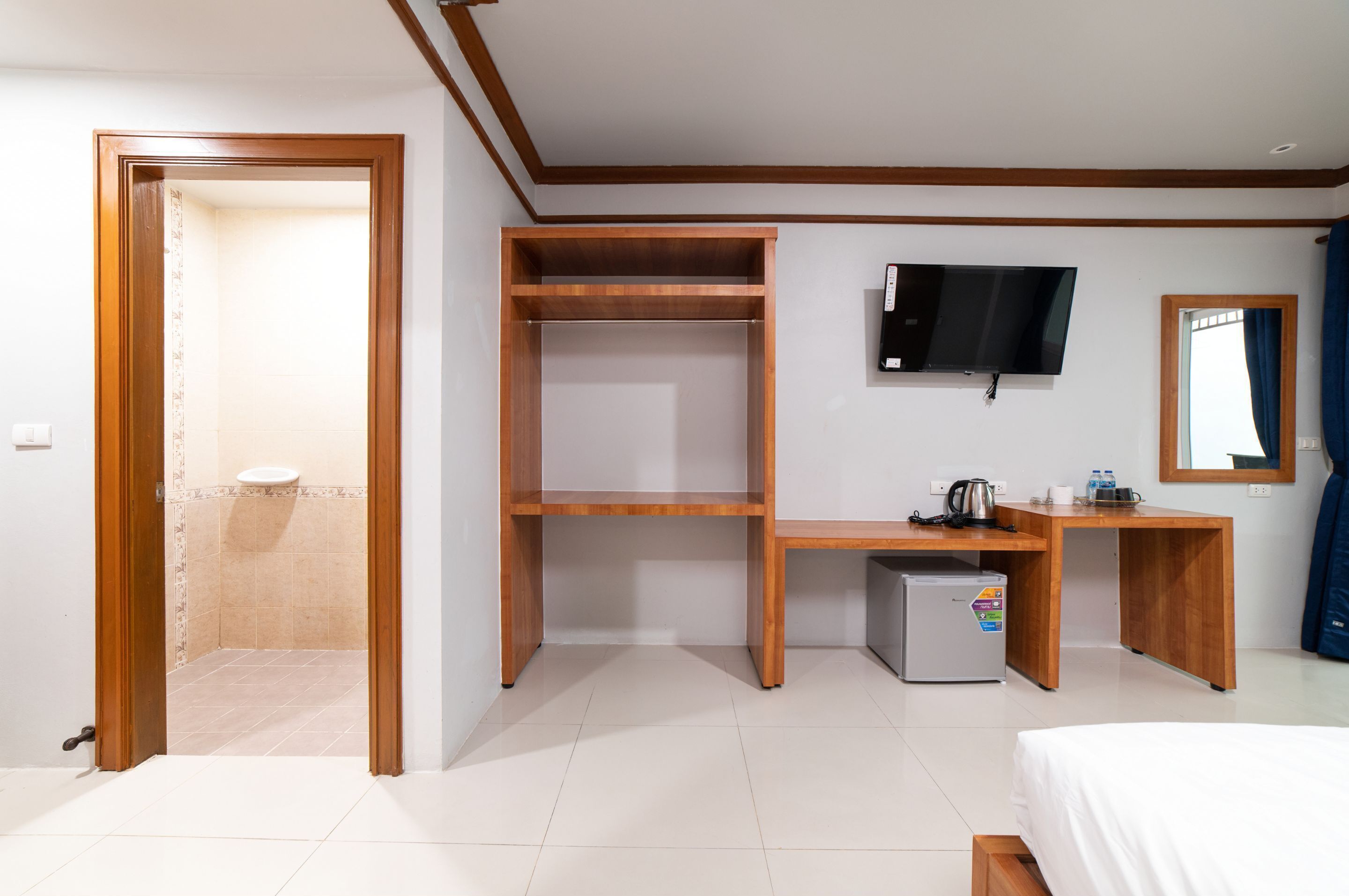 Quarto de hotel com escrivaninha de madeira, televisão, pequeno frigorífico e uma cama.