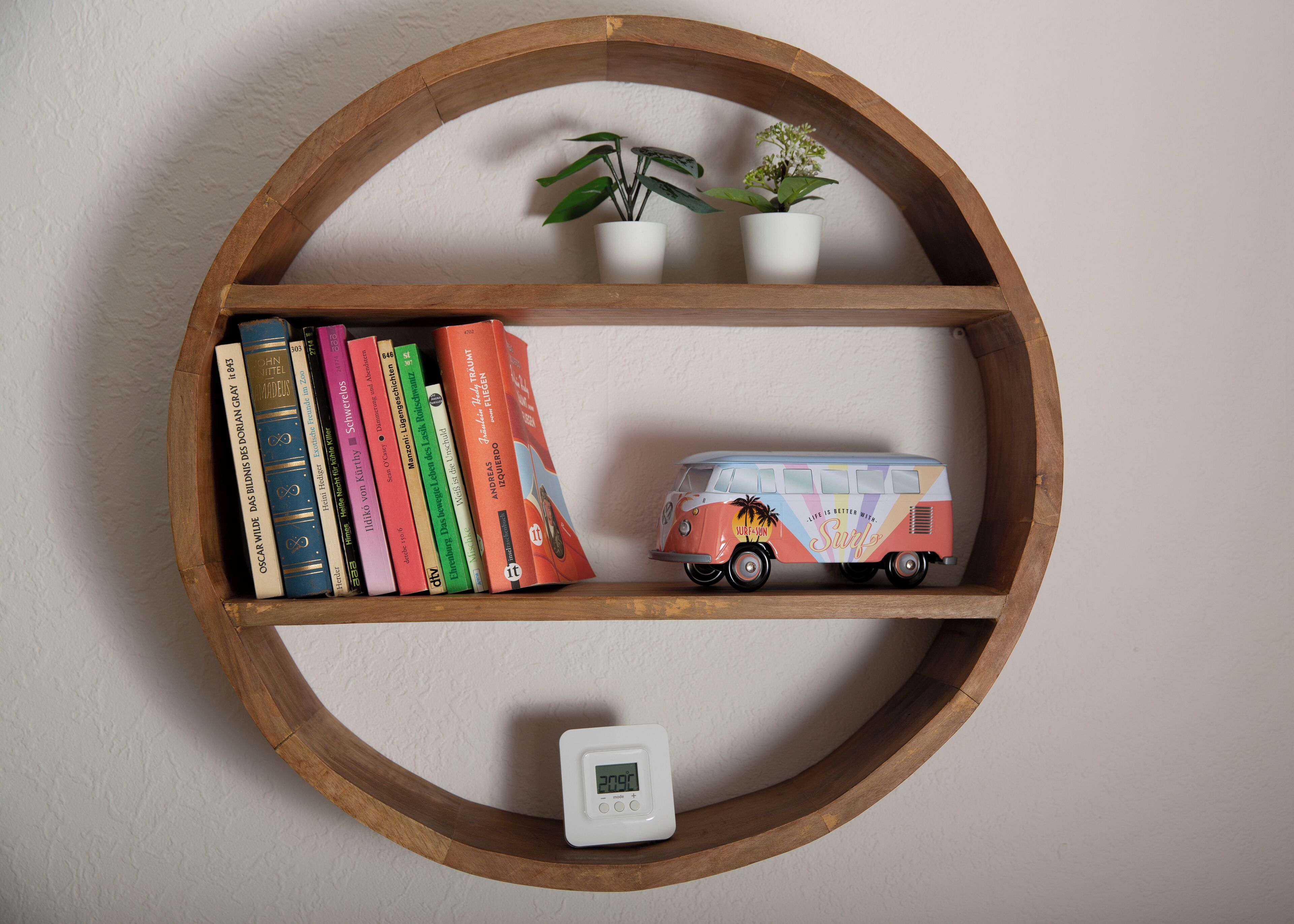 A wooden shelf with books, a small plant, a toy van, and a thermostat.