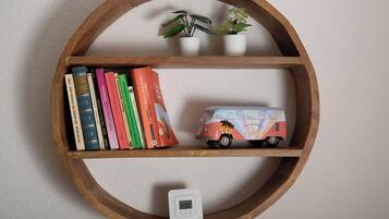 Una estantería de madera con libros, una planta pequeña, un camión de juguete y un termostato.