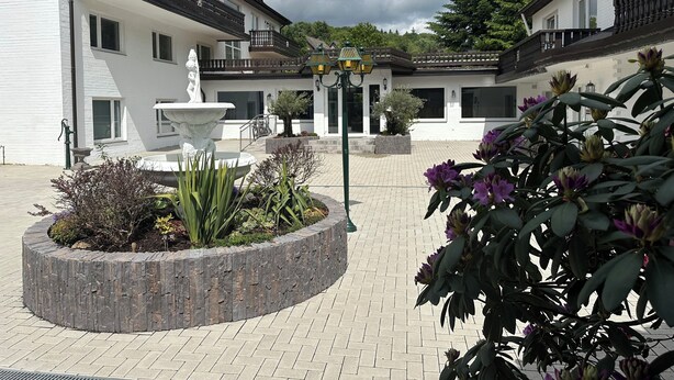 A courtyard with a fountain, potted plants, and a building with balconies. - Hotel Waldberg (Stolberg)