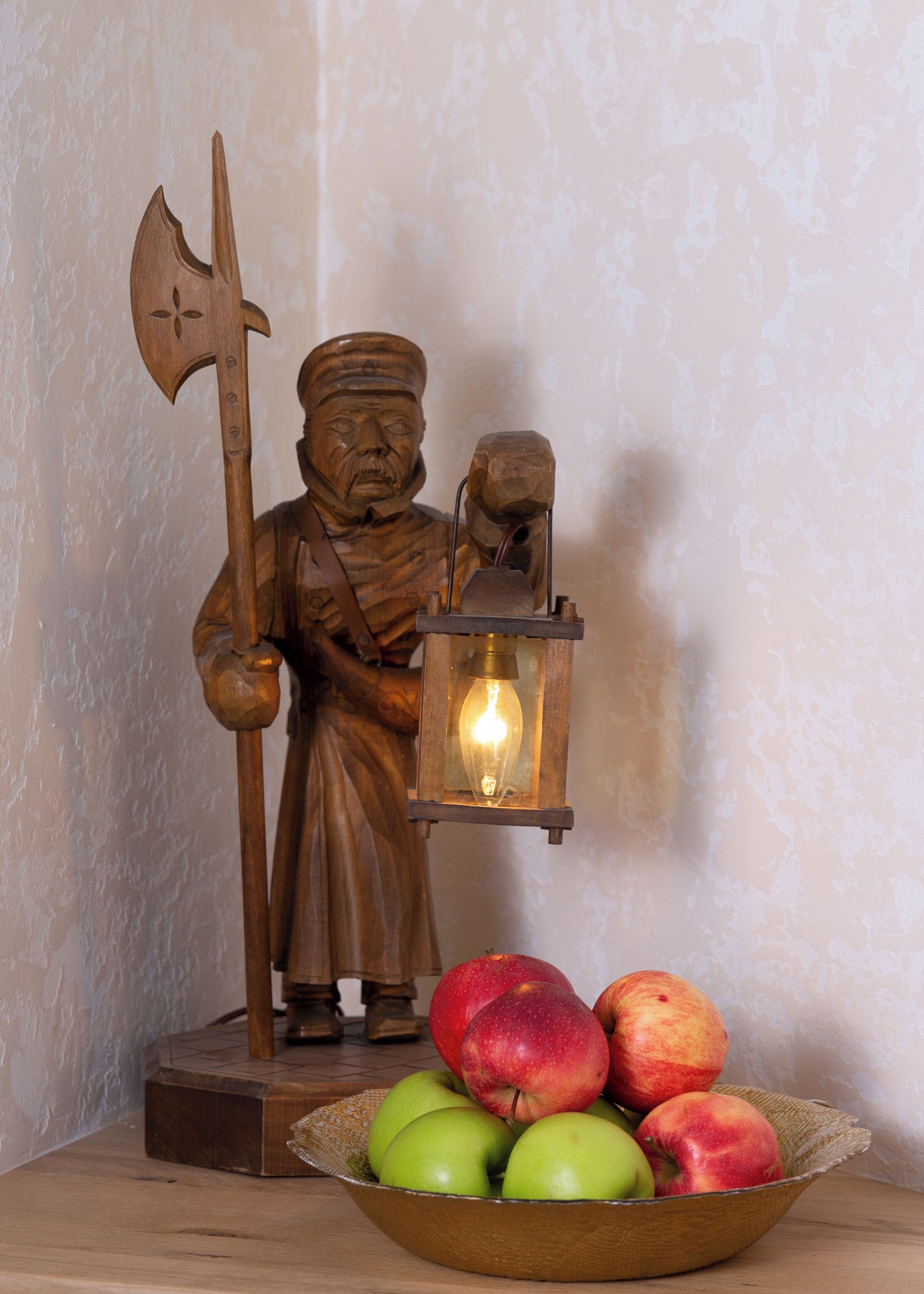 A wooden statue of a figure holding an axe and a lantern, with a bowl of apples in front.