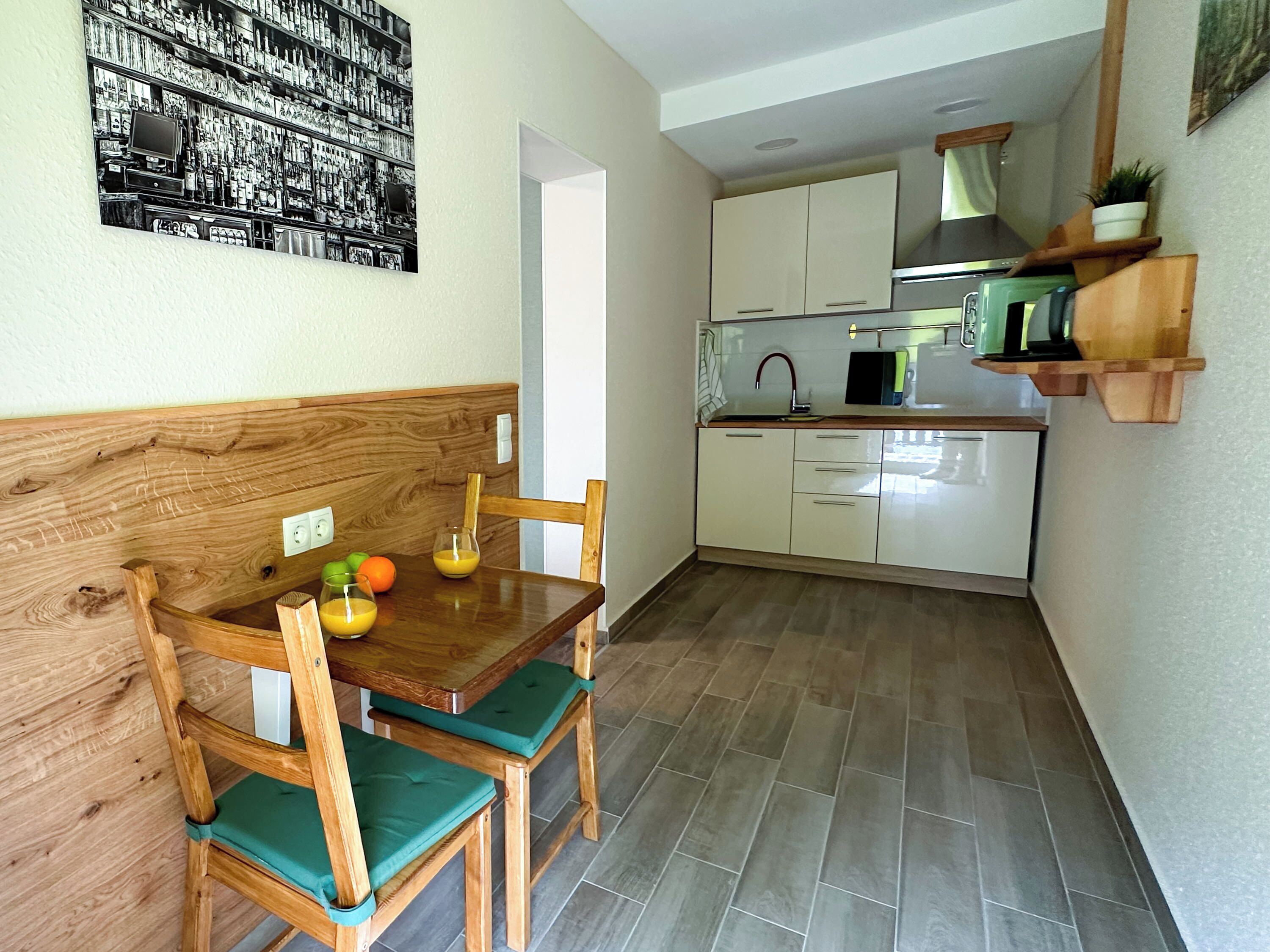 Une petite cuisine avec une table à manger en bois, des chaises et une étagère fixée au mur.
