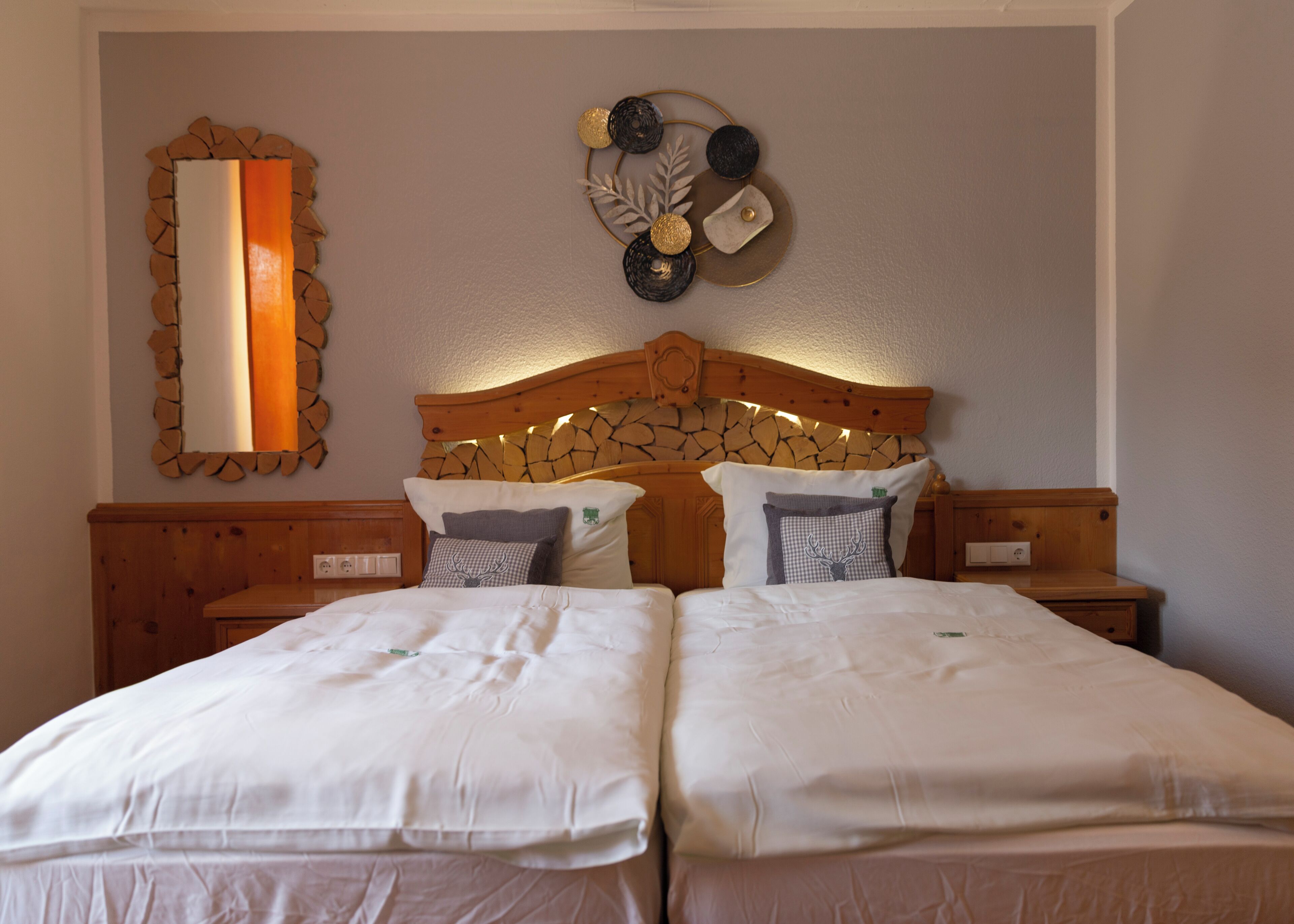 A double bed with white linens, a wooden headboard with a stone pattern, and two bedside tables with lamps.