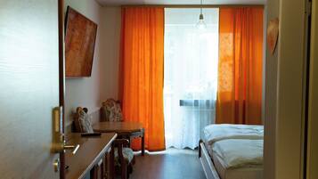 Une chambre d’hôtel avec un plancher en bois, un lit, un bureau avec une chaise et un téléviseur fixé au mur.