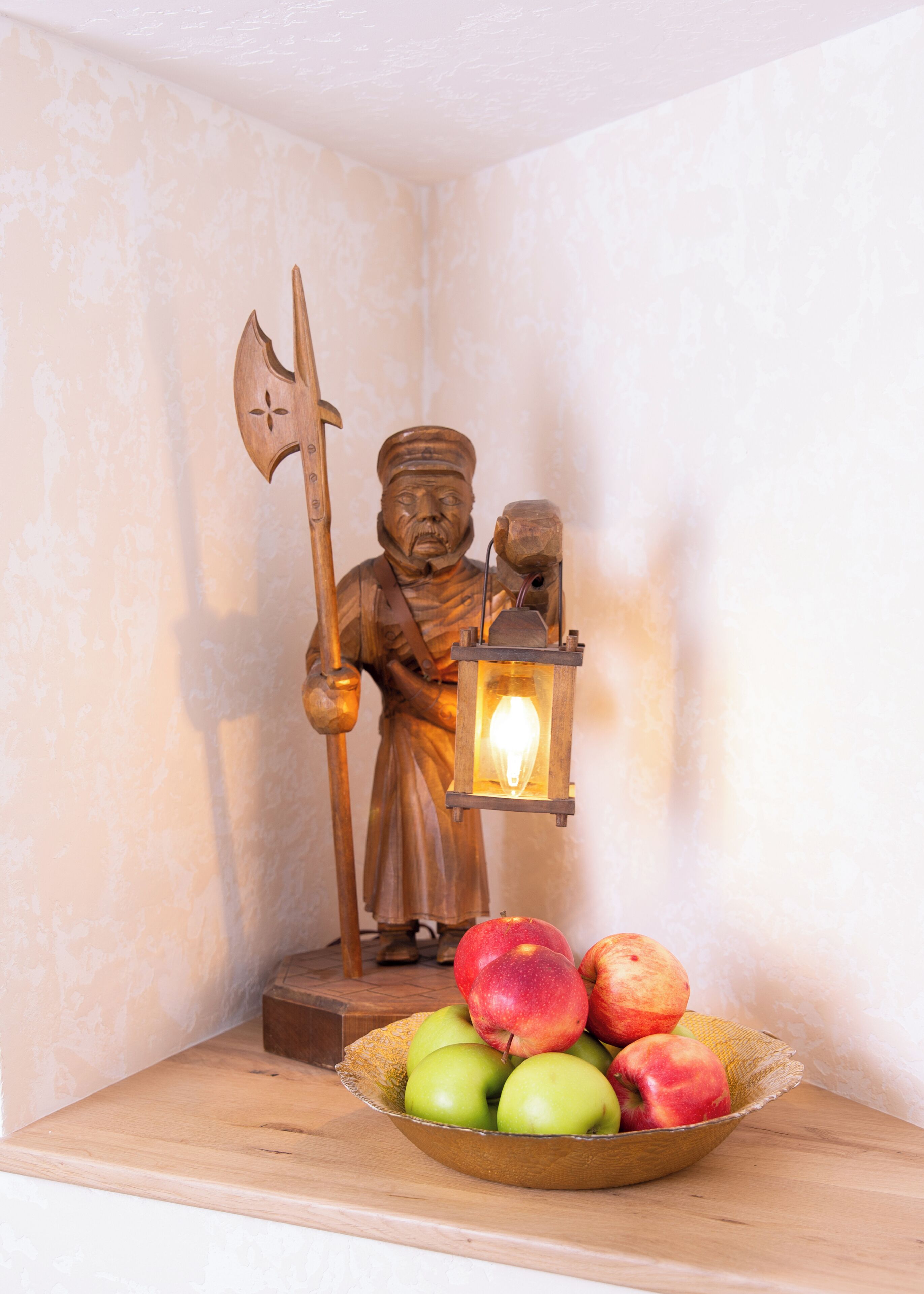 Una estatua de una figura sosteniendo un hacha y un farol, con un cuenco de manzanas al frente.