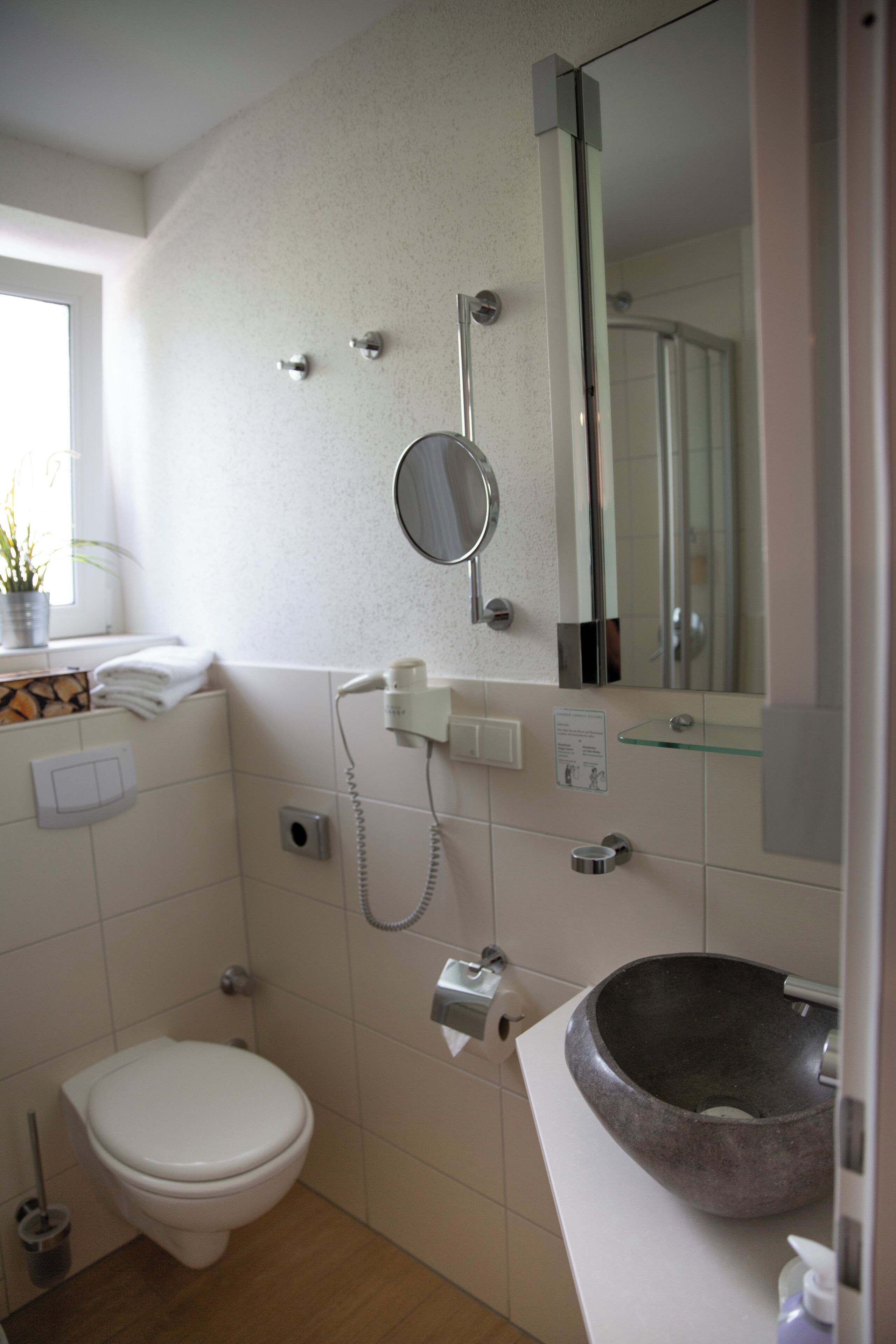 A bathroom with a toilet, a sink with a stone basin, a mirror, and a shower.