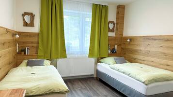 A room with two single beds, a window with sheer curtains, a radiator, and wooden headboards.