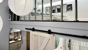 A modern bedroom with a large bed, a wooden door, and a view of the kitchen. - Sebastiana 22/7 (Kraków)