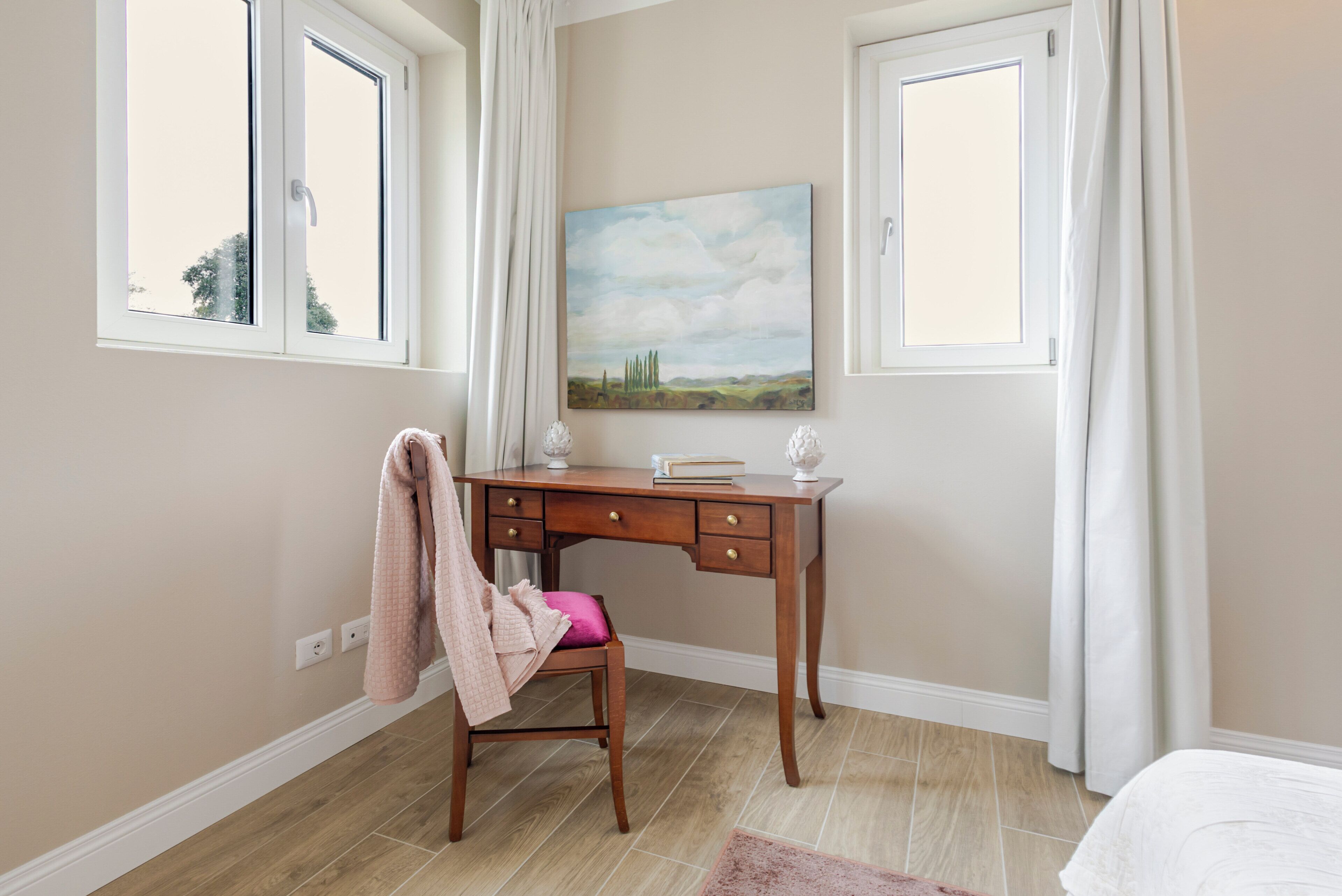 Een slaapkamer met een houten bureau, een stoel, een bed en een schilderij aan de muur.