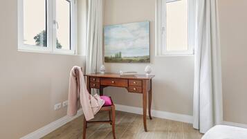 Een slaapkamer met een houten bureau, een stoel, een bed en een schilderij aan de muur.
