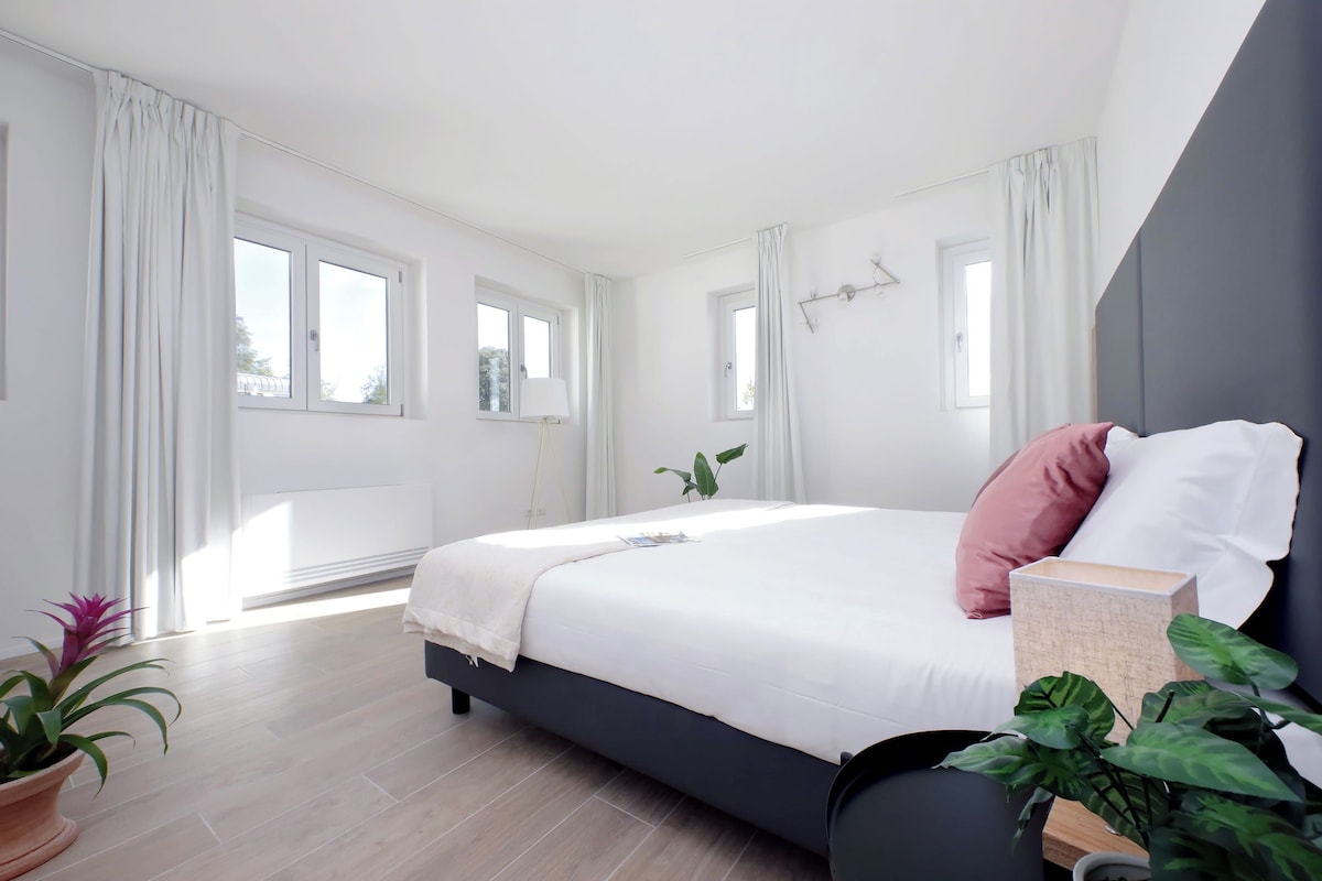 A modern bedroom with a large bed, a bedside table, and a window.