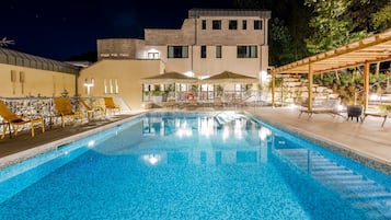 A swimming pool with lounge chairs and umbrellas, surrounded by a building with a stone facade and a covered outdoor seating area.