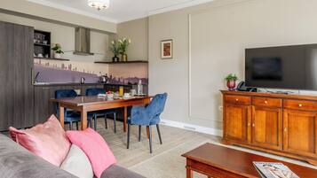 A modern living room with a sofa, a coffee table, a TV, a dining area with chairs, and a kitchen with a stove.