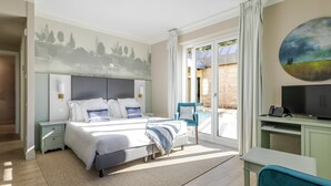 A bedroom with a bed, bedside tables, a desk, a chair, a TV, and a painting on the wall. - Guild Living Siena Senior Resort & Residence (Siena)