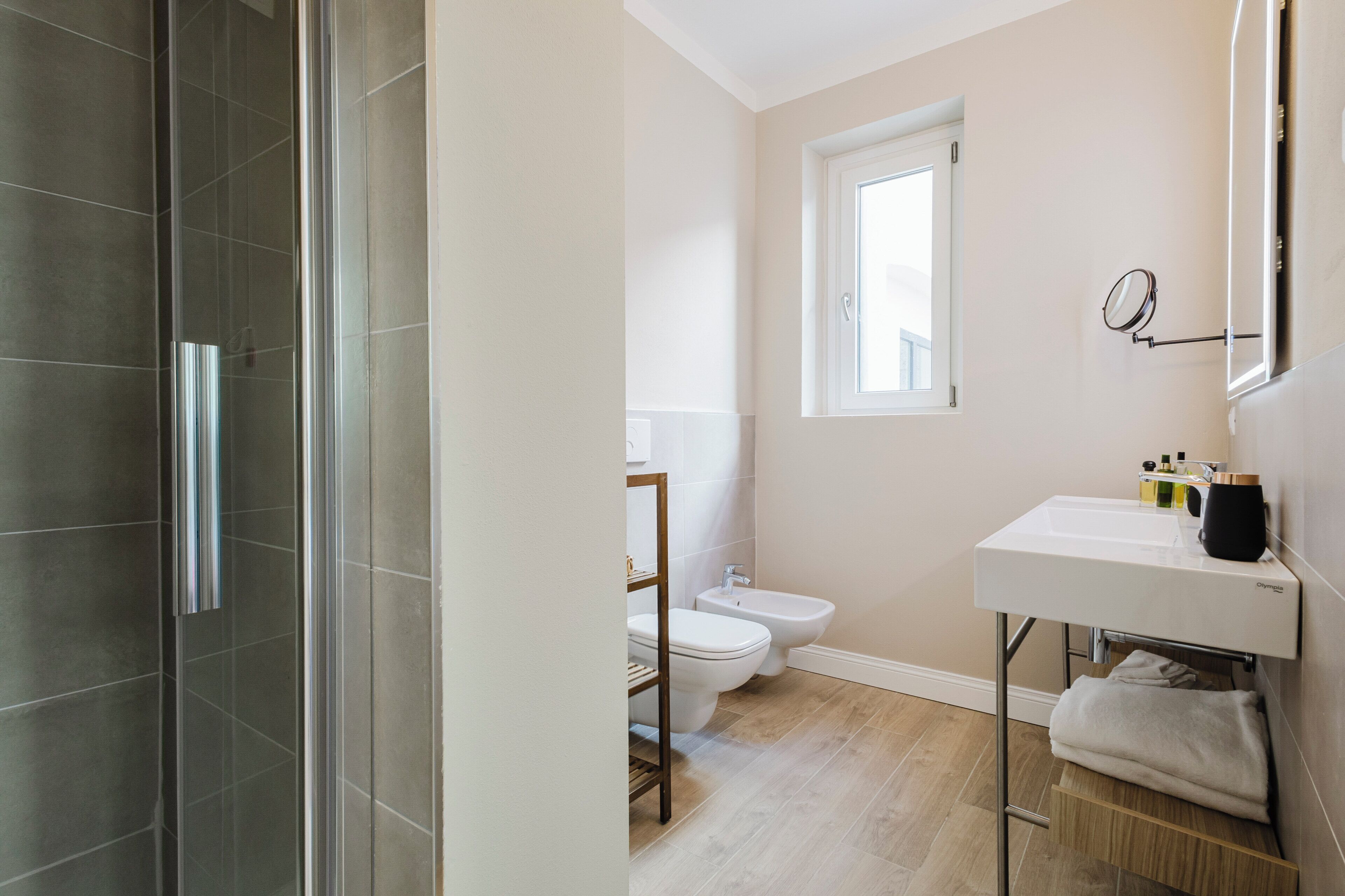 A bathroom with a shower, toilet, bidet, and a sink with a mirror.