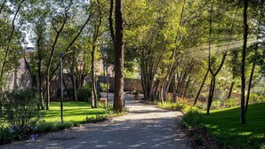 A gravel pathway flanked by trees and greenery, leading to a building with a stone wall. - Guild Living Siena Senior Resort & Residence (Siena)