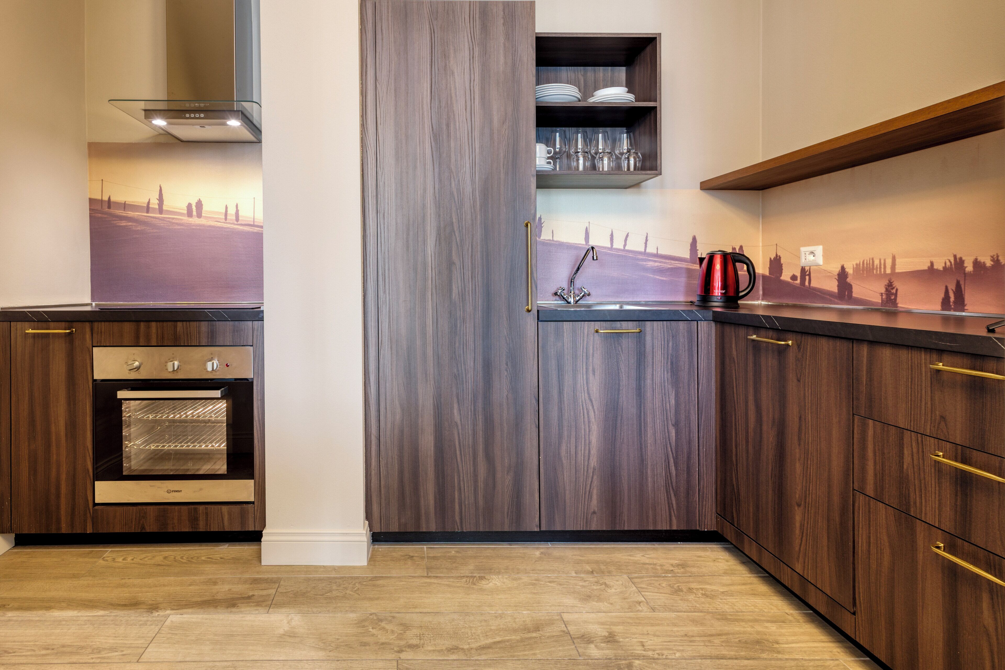 A kitchen with wooden cabinets, a built-in oven, a stainless steel sink, and a red kettle.