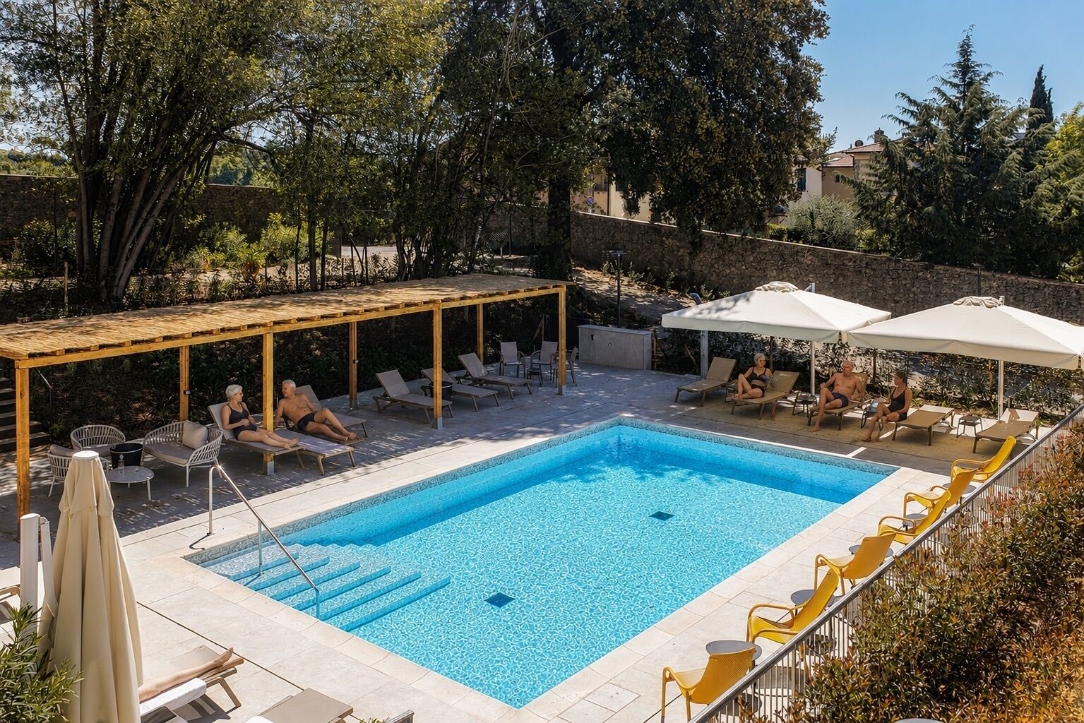 Una piscina rettangolare con una pergola in legno e poltrone prendisole intorno.
