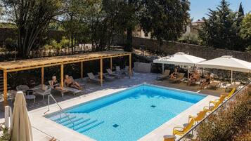 Una piscina rettangolare con una pergola in legno e poltrone prendisole intorno.