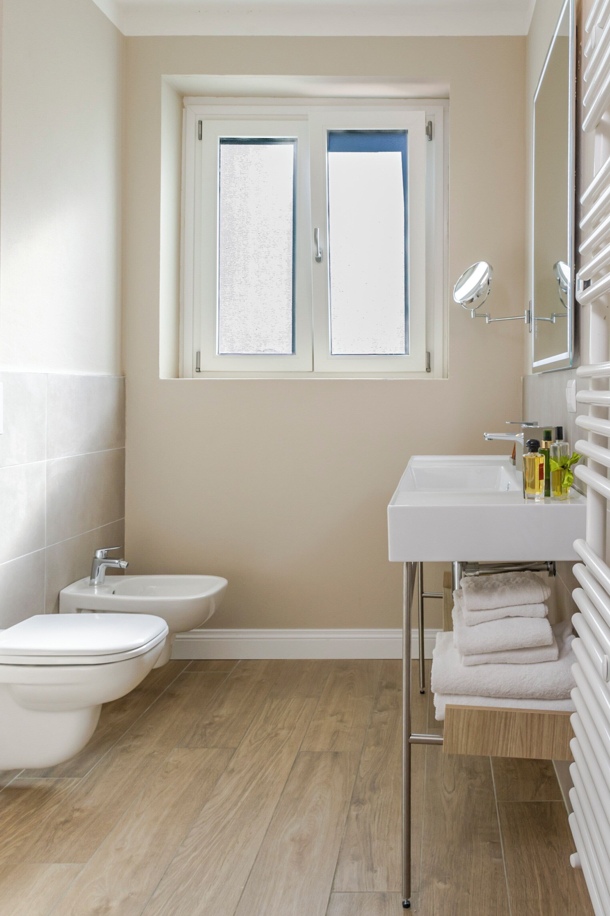 Une salle de bain comprenant des toilettes, un bidet, un lavabo blanc et une fenêtre située au-dessus du lavabo.
