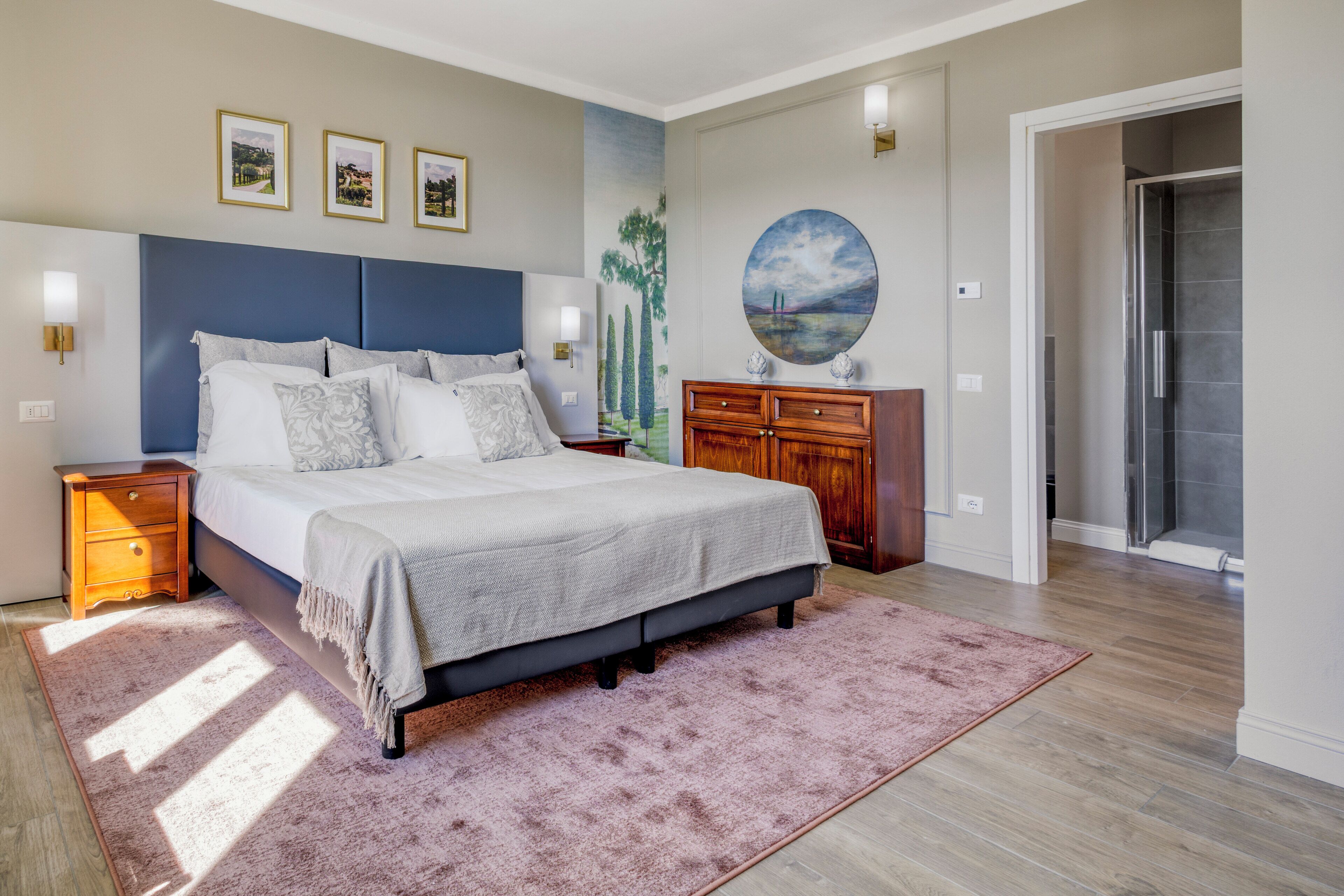 A bedroom with a bed, nightstands, a dresser, a painting, and a shower.