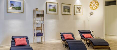 A room with four reclining chairs, a shelf with towels, and framed pictures on the wall.